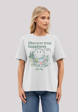 White cotton t-shirt featuring a graphic with a smiling face, flowers, and greenery. Text reads, "Discover true happiness when you go outdoors."