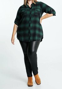 Zielono-czarna koszula w kratę na guziki z długimi rękawami, z dwoma kieszeniami na piersi, w zestawieniu z czarnymi skórzanymi legginsami i beżowymi botkami za kostkę.