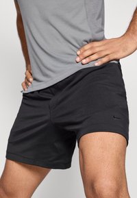 Fekete sportnadrág könnyű anyagból, sima felülettel, rugalmas derékrésszel és egy kis logóval az alján.