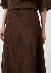 Gonna in suede marrone con una texture liscia, forma leggermente svasata e dettagli in pannello. Il tessuto ha una finitura morbida e opaca.