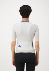 White athletic shirt with short sleeves, mesh texture, blue accents, and a zippered pocket at the back, designed for performance wear.