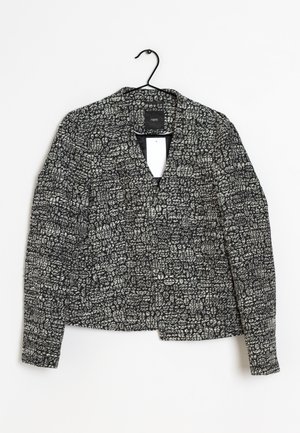 Zwart-witte, gestructureerde damesblazer met lange mouwen, open voorkant en ingesneden kraag, hangend aan een zwarte hanger.