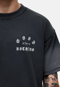 T-shirt noir surdimensionné en tissu doux avec un texte graphique blanc "GOD for NOTHING" dans une police stylisée à l'avant.
