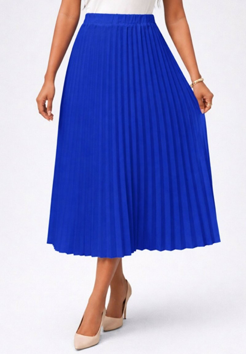 Femme portant une jupe midi plissée bleu vif associée à des talons hauts beiges et un haut blanc, debout devant un fond uni.