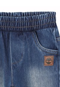 Pantaloni in denim con vita elastica, caratterizzati da un lavaggio azzurro chiaro, sei tasche e un'etichetta logo in pelle marrone sul fronte.