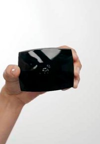 Objet rectangulaire noir tenu dans une main, surface brillante, bords légèrement courbés, présentant un motif central en relief.