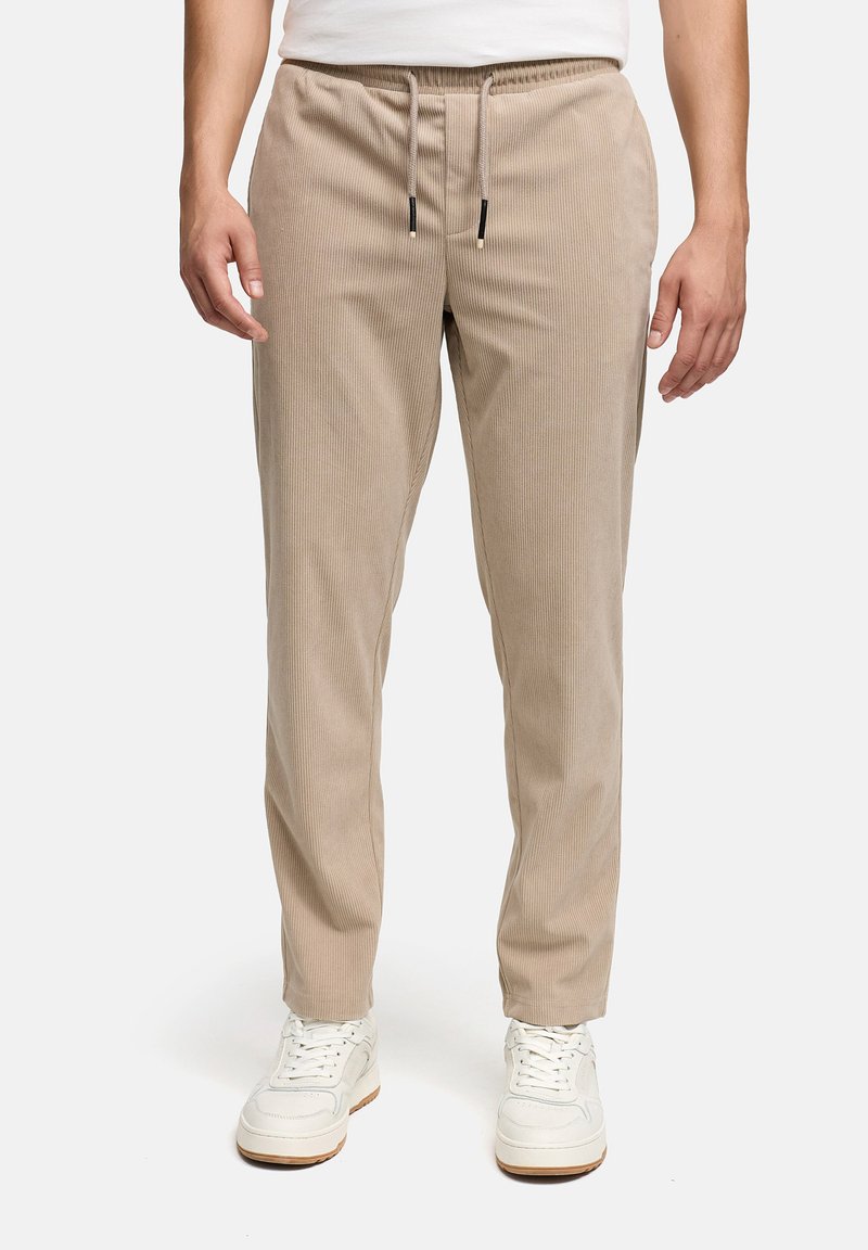 Pantaloni beige in velluto a coste con vita con coulisse e tasche laterali, abbinati a sneakers bianche. Tessuto liscio e design a gamba dritta.