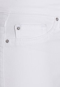 Vitt denimtyg med metallnitar och detaljerad sömnad runt en liten och en stor ficka.