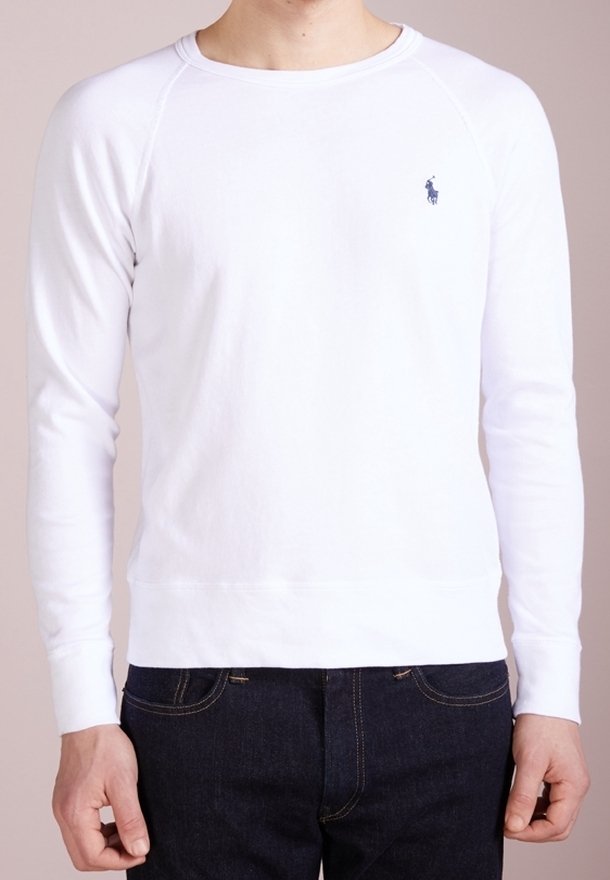 Homme portant un t-shirt blanc uni à manches longues avec un petit logo bleu foncé sur la poitrine et un jean bleu foncé.