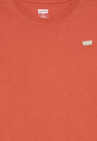 Rostfärgad bomulls t-shirt med rund halsringning. Har en liten beige Levi's-logotyp på övre vänstra sidan. Slät textur.