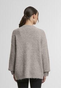Svetlo siva pletena pulover z ohlapnim krojem, spuštenimi rameni in teksturirano tkanino. Rob je nekoliko daljši zadaj.