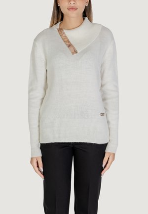 Maglione bianco lavorato a maglia con un colletto asimmetrico unico, caratterizzato da un accento a motivo beige e polsini a coste, abbinato a pantaloni neri.