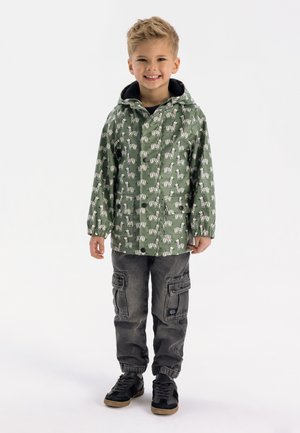 Groene regenjas met een patroon van zebra-ontwerpen, voorzien van een zwarte capuchon, gecombineerd met grijze cargo-broeken en zwarte sneakers.