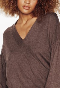 Pull en tricot marron avec un décolleté en V profond, des manches surdimensionnées et une texture subtile. Le tissu semble doux et confortable.