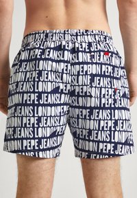 Morske šorts za plivanje s bijelim tekstualnim uzorkom koji sadrži "Pepe Jeans London." Elastična waistband i dva stražnja džepa s crvenim naglascima.