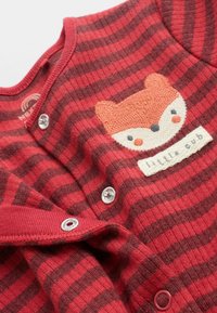 Röd- och brunspräcklig långärmad bodysuit med en applikation av en räv, tryckknappar och en etikett med "litet ungt djur" på en texturerad lapp.