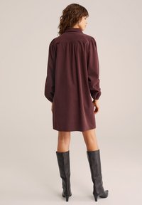 Abito lungo bordeaux con colletto, schiena arricciata, vestibilità rilassata e maniche a palloncino; abbinato a stivali neri con tacco al ginocchio.