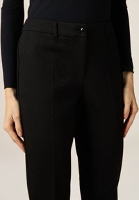 Černé kalhoty na míru s hladkou texturou, zdobené posádkou kamínků a předním zapínáním na knoflík.