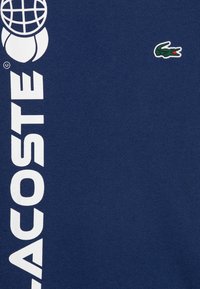 Marineblauwe T-shirt gemaakt van zachte katoen met witte "LACOSTE" tekst en een klein groen krokodillenlogo op de borst. Soepele textuur.