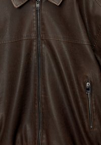 Braune Lederjacke mit Reißverschluss, spitzem Kragen und seitlicher Tasche mit Metallreißverschluss. Glatte Textur und weiches Finish.