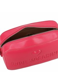 Borsa cosmetica in ecopelle rosa con chiusura a zip, logo in rilievo, dettaglio a forma di cuore e fodera interna marrone.