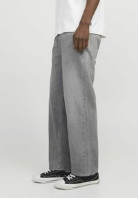 Jean large gris en denim, doté d'un design classique à cinq poches. Porté avec des baskets noires, mettant en avant un look décontracté.