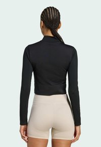 Black cropped long-sleeve top with a smooth texture and mock collar, paired with beige textured high-waisted shorts.