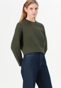 Maglione corto verde oliva con collo rotondo e texture a coste. Abbinato a jeans in denim blu scuro a vita alta.