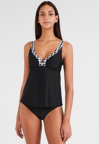 Zwart zwemtop met een diepe V-hals en geruite rand. Heeft verstelbare bandjes en een relaxte pasvorm. Gecombineerd met zwarte bikini-bottoms.