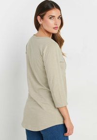 Helle beige Langarm-Bluse mit Rundhalsausschnitt, in lockerer Passform und weichem Material, kombiniert mit dunkelblauen Jeans.
