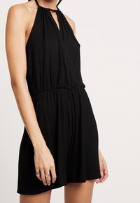 Svart halterneck-romper i mjukt material, med en nyckelhålsringning, samlad midja och avslappnade shorts med en slät yta.