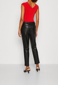 Červený upnutý body s V-zadním výstřihem, kombinovaný s černými koženými zúženými kalhotami. Černé sandály na vysokém podpatku dokončují vzhled.