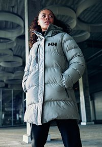 Dikke, lichtgrijze parka met een hoge kraag, rits sluiting, zijzakken en een zwart logo "HH" op de linkerkant van de borst.