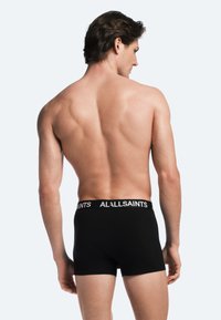 Boxer briefs de algodón negro con una cinturilla blanca con el logo "ALLSAINTS", diseño ajustado y textura suave. Modelo visto desde atrás.