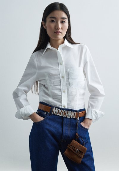 Λευκό πουκάμισο με κωδικό μπροστά, συνδυασμένο με μπλε τζιν και καφέ δερμάτινη ζώνη με λογότυπο MOSCHINO. Επίσης, υπάρχει μια μικρή καφέ τσάντα αξεσουάρ.