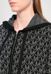 Black zip-up hoodie with geometric gray pattern, contrasting gray fabric on the hood. Soft texture and ribbed cuffs complete the design.