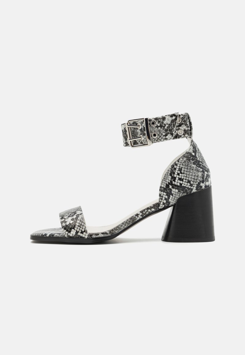 Black and white snake print heeled sandal with a square toe, adjustable ankle strap, and a chunky black heel. Smooth texture throughout.