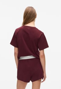 Bordeaux katoenen T-shirt met korte mouwen, een licht cropped ontwerp, gecombineerd met bijpassende shorts met een grijze elastische tailleband.