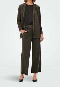 Giacca su misura di colore verde scuro con pantaloni a gamba larga coordinati, abbinati a un top nero. Tessuto liscio con una sottile texture e accenti neutri.