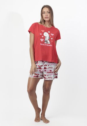 Mujer vistiendo una camiseta roja con Snoopy y Woodstock abrazándose, rodeados de corazones y texto "Mejores amigos", combinada con pantalones cortos estampados con tiras cómicas.