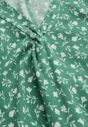 Grüner Stoff mit weißem Blumenmuster mit kleinen Blumen und Blättern, an einer zentralen Naht mit sichtbaren Nähten gerafft.