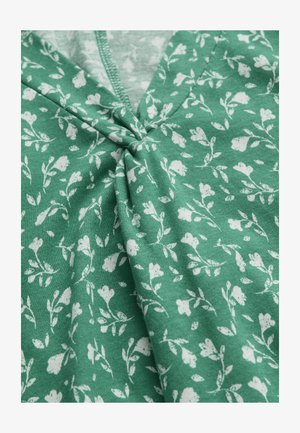 Grüner Stoff mit weißem Blumenmuster mit kleinen Blumen und Blättern, an einer zentralen Naht mit sichtbaren Nähten gerafft.