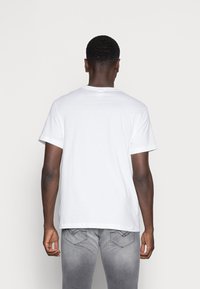 Camiseta blanca de algodón con cuello redondo, mangas cortas y un corte relajado. Textura suave y sin gráficos ni patrones visibles.
