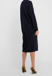 Marinblå stickad klänning med en lös passform, knälång, lång ärm, ribbade manschetter, kombinerad med gula och svarta mönstrade klackskor.