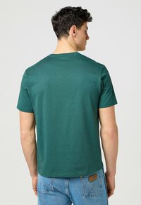 Grön bomullströja med korta ärmar och rund halsringning, med en mjuk textur och rak passform, tillsammans med blå denimjeans.