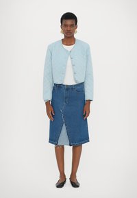 Jachetă matlasată bleu deschis cu nasturi rotunzi, asociată cu o fustă din denim bleu închis, cu o deschidere frontală și margini nefinisate, completată de pantofi negri.