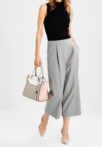 Grijze wijde broek met zijzakken, gecombineerd met een zwarte mouwloze top. Houdt een multi-kleurige handtas vast in grijs, wit en roze. Schoenen zijn lichtroze.