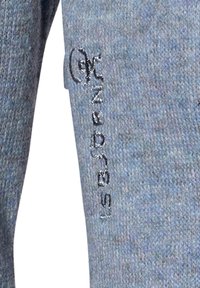 Gråblå strikbukser med en subtil tekstur, vertikale syninger og et broderet logo på venstre ben.