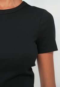 Μαύρο ριμπ κοντομάνικο μπλουζάκι με στρογγυλή λαιμόκοψη. Το ύφασμα έχει λεία υφή με διακριτικές κάθετες γραμμές.