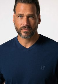 Camiseta de cuello en v de color azul marino, hecha de una tela suave con un sutil acento de logo en el pecho, que presenta un corte clásico y una textura suave.